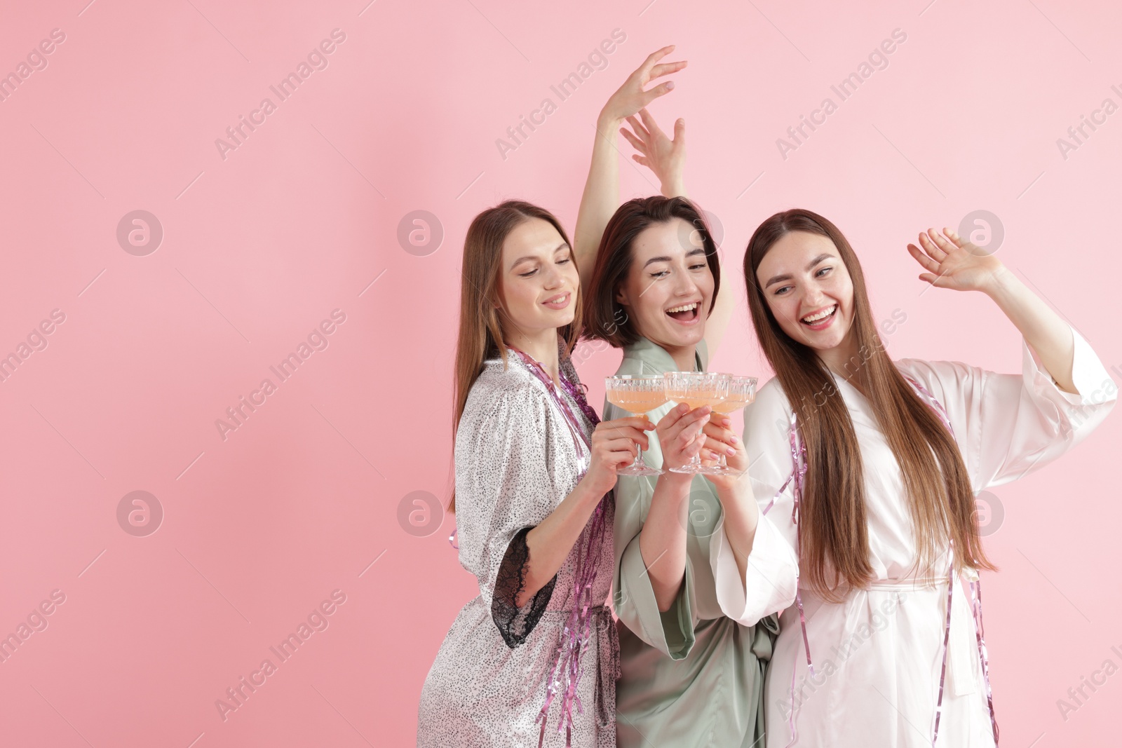 Photo of Pajama party. Happy friends with tinsel clinking glasses on pink background. Space for text