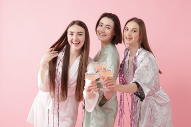 Photo of Pajama party. Happy friends with tinsel clinking glasses on pink background