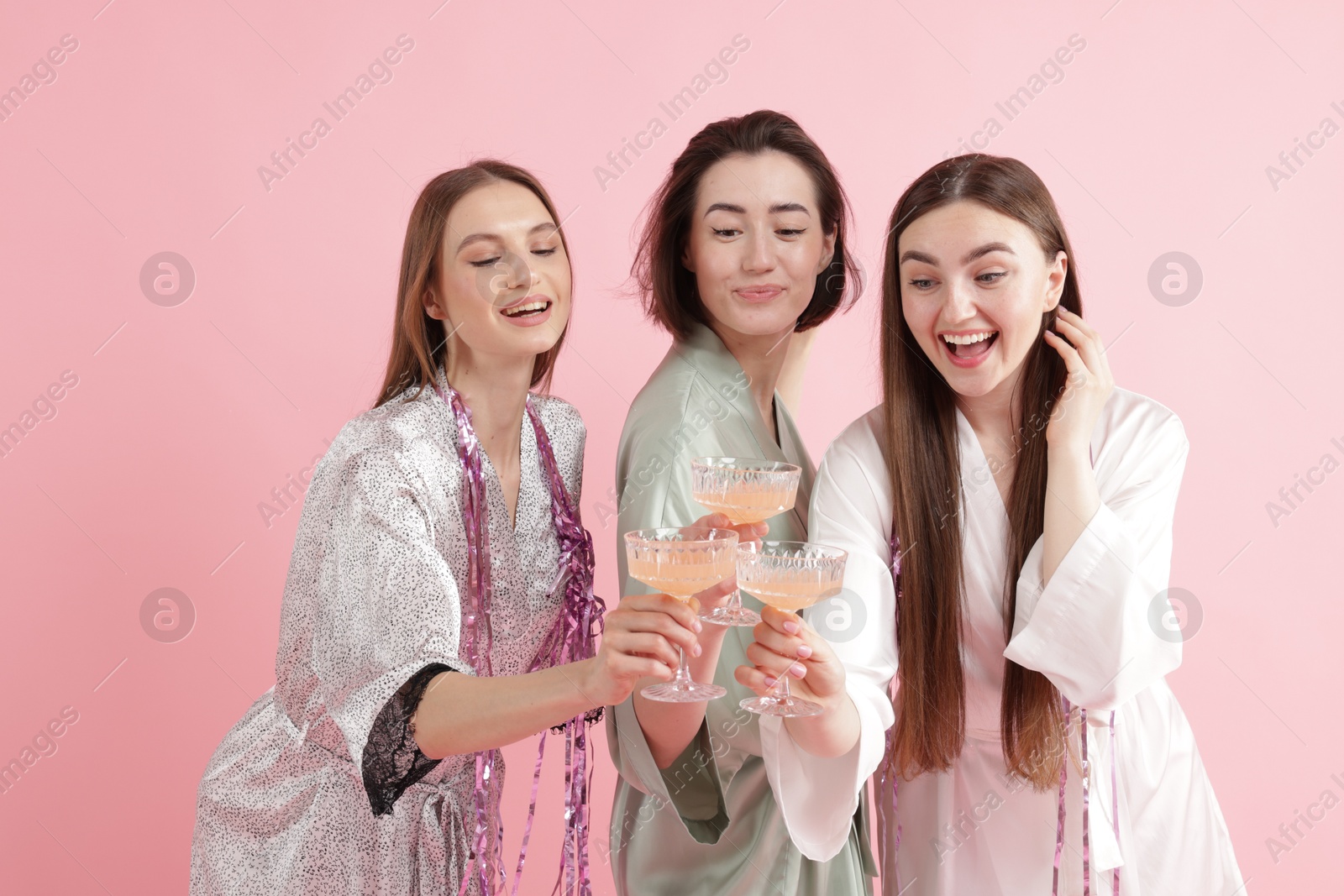 Photo of Pajama party. Happy friends with tinsel clinking glasses on pink background