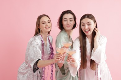 Photo of Pajama party. Happy friends with tinsel clinking glasses on pink background
