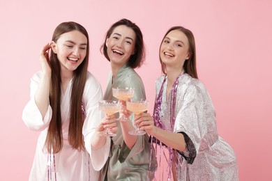 Photo of Pajama party. Happy friends with tinsel clinking glasses on pink background