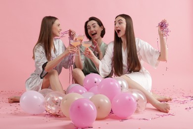 Photo of Pajama party. Happy friends with tinsel and balloons clinking glasses on pink background