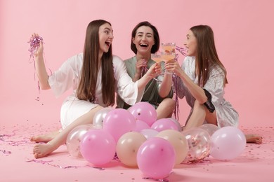 Photo of Pajama party. Happy friends with tinsel and balloons clinking glasses on pink background