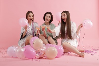 Photo of Pajama party. Happy friends with tinsel and balloons clinking glasses on pink background
