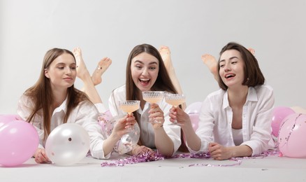 Photo of Pajama party. Happy friends with tinsel and balloons clinking glasses on grey background