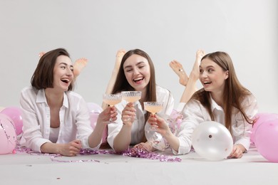 Photo of Pajama party. Happy friends with tinsel and balloons clinking glasses on grey background