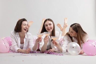 Photo of Pajama party. Happy friends with tinsel and balloons clinking glasses on grey background