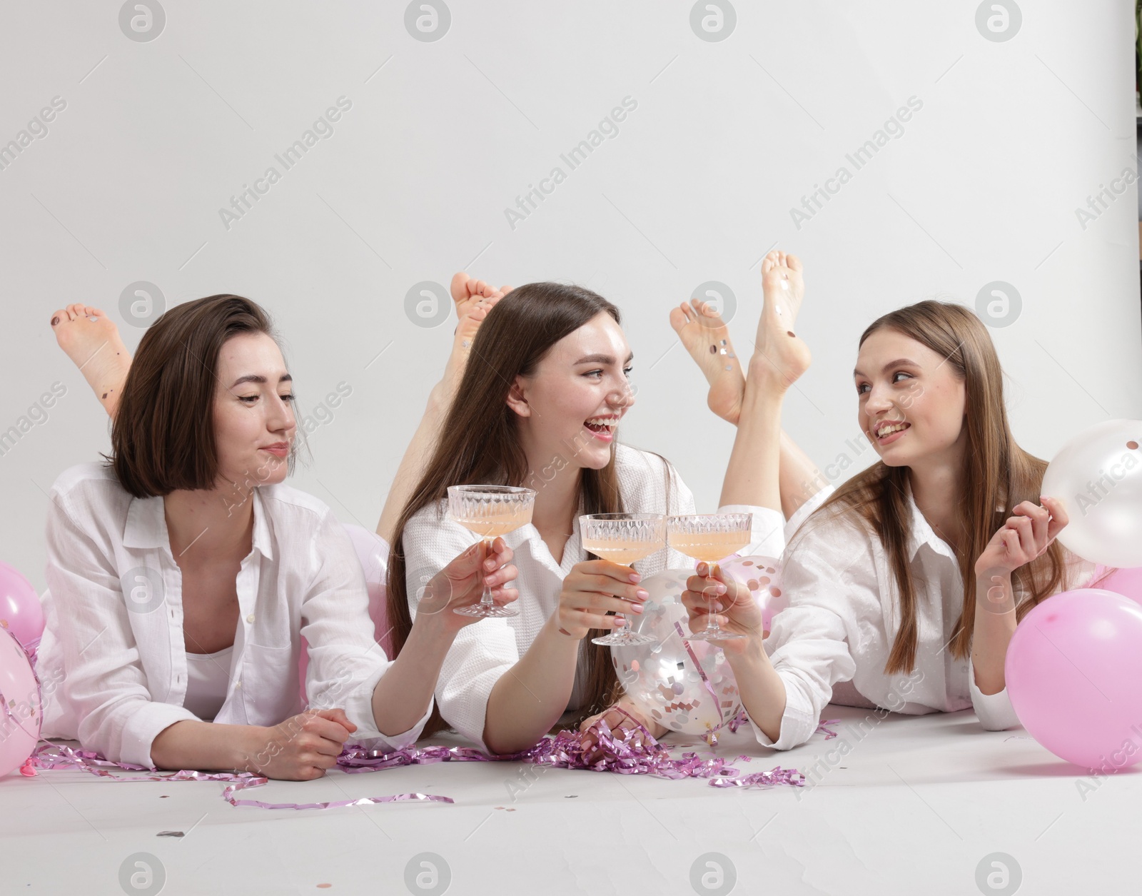 Photo of Pajama party. Happy friends with tinsel and balloons clinking glasses on grey background