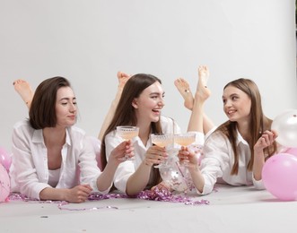 Photo of Pajama party. Happy friends with tinsel and balloons clinking glasses on grey background