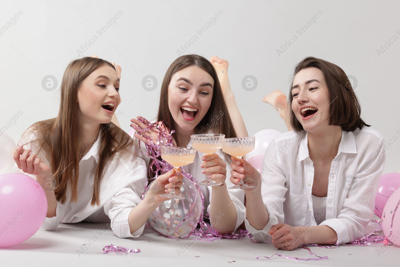 Photo of Pajama party. Happy friends with tinsel and balloons clinking glasses on grey background
