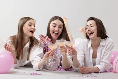 Photo of Pajama party. Happy friends with tinsel and balloons clinking glasses on grey background