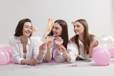 Photo of Pajama party. Happy friends with tinsel and balloons clinking glasses on grey background