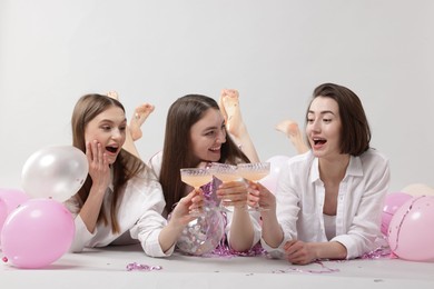 Photo of Pajama party. Happy friends with tinsel and balloons clinking glasses on grey background