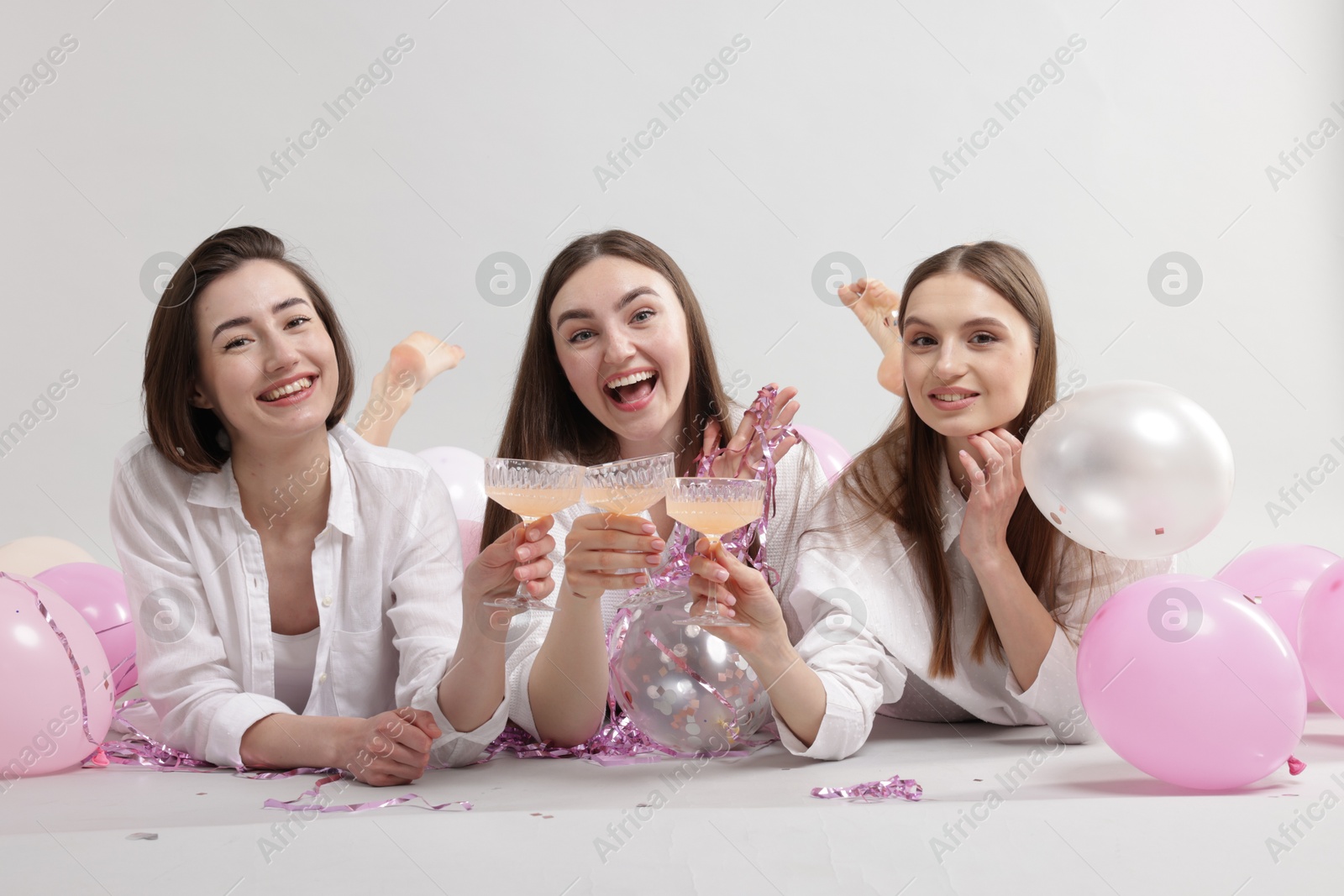 Photo of Pajama party. Happy friends with tinsel and balloons clinking glasses on grey background