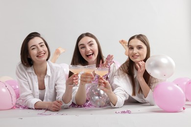 Photo of Pajama party. Happy friends with tinsel and balloons clinking glasses on grey background