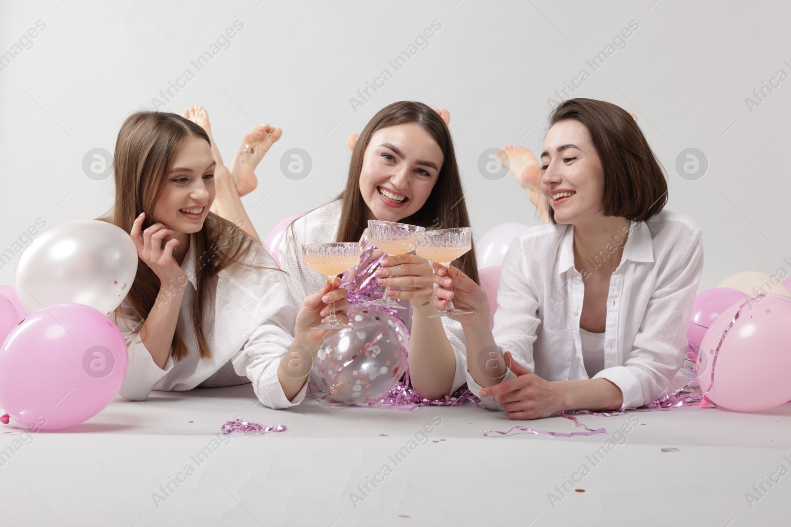 Photo of Pajama party. Happy friends with tinsel and balloons clinking glasses on grey background