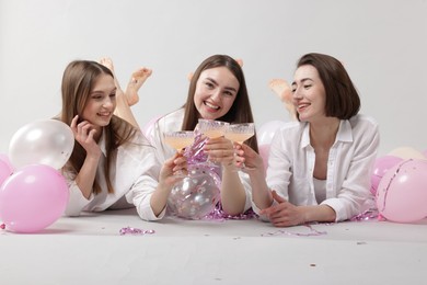 Photo of Pajama party. Happy friends with tinsel and balloons clinking glasses on grey background