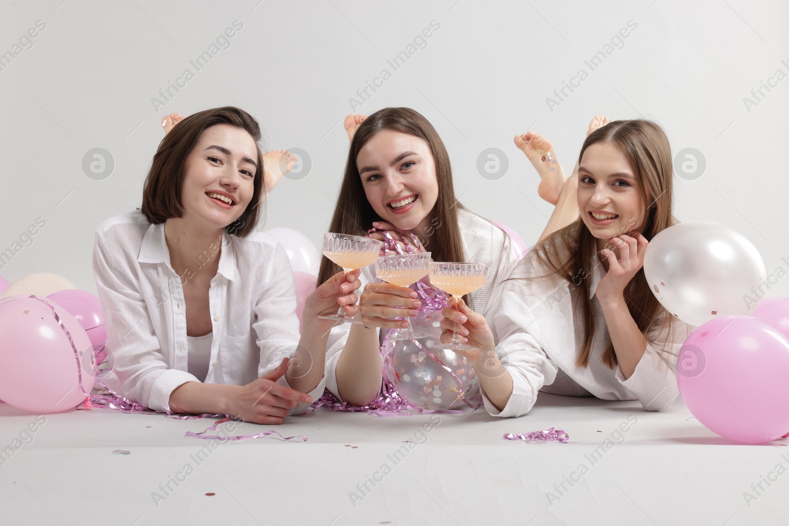 Photo of Pajama party. Happy friends with tinsel and balloons clinking glasses on grey background