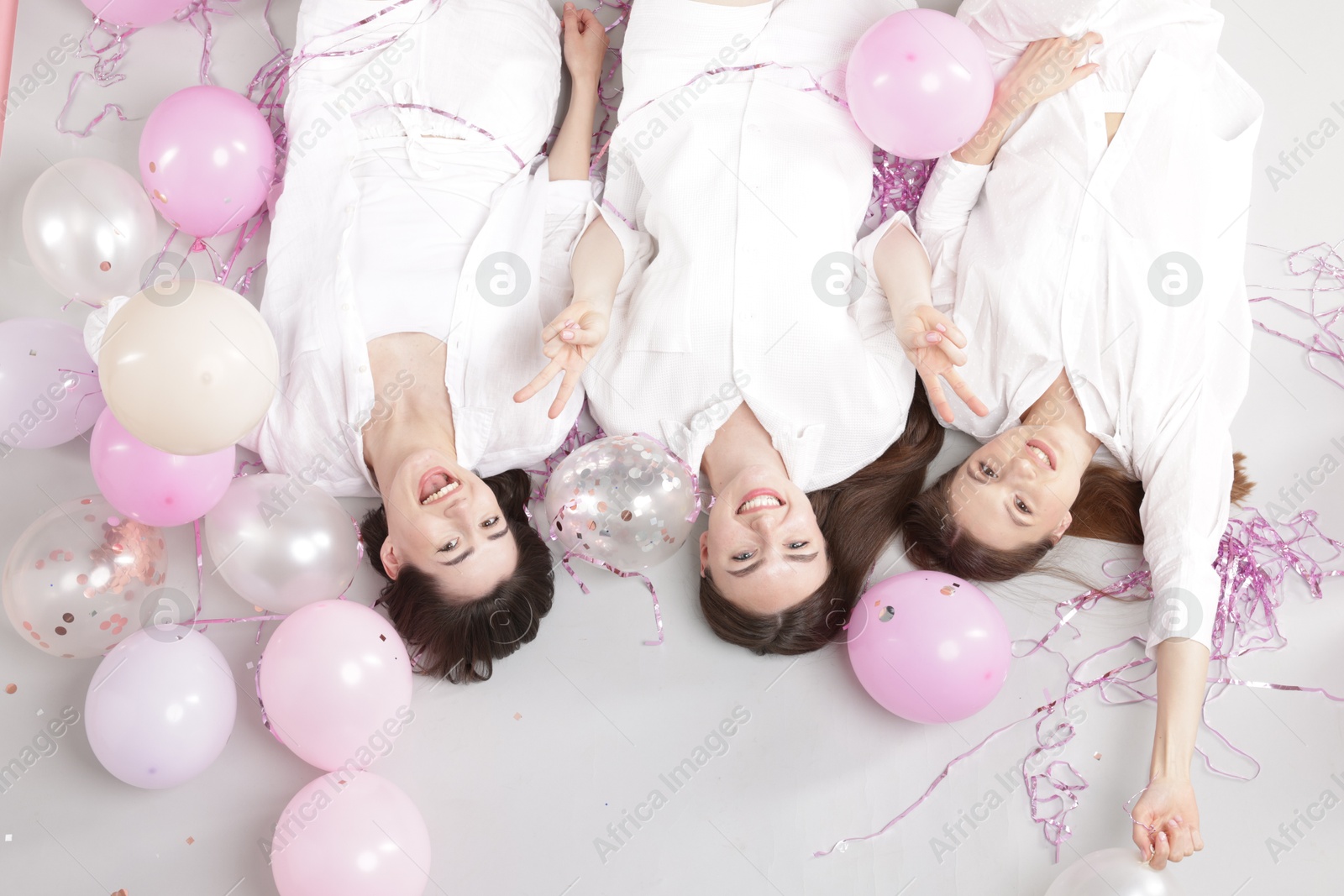 Photo of Pajama party. Happy friends with balloons and tinsel on grey background, above view
