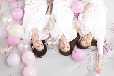 Photo of Pajama party. Happy friends with balloons and tinsel on grey background, above view