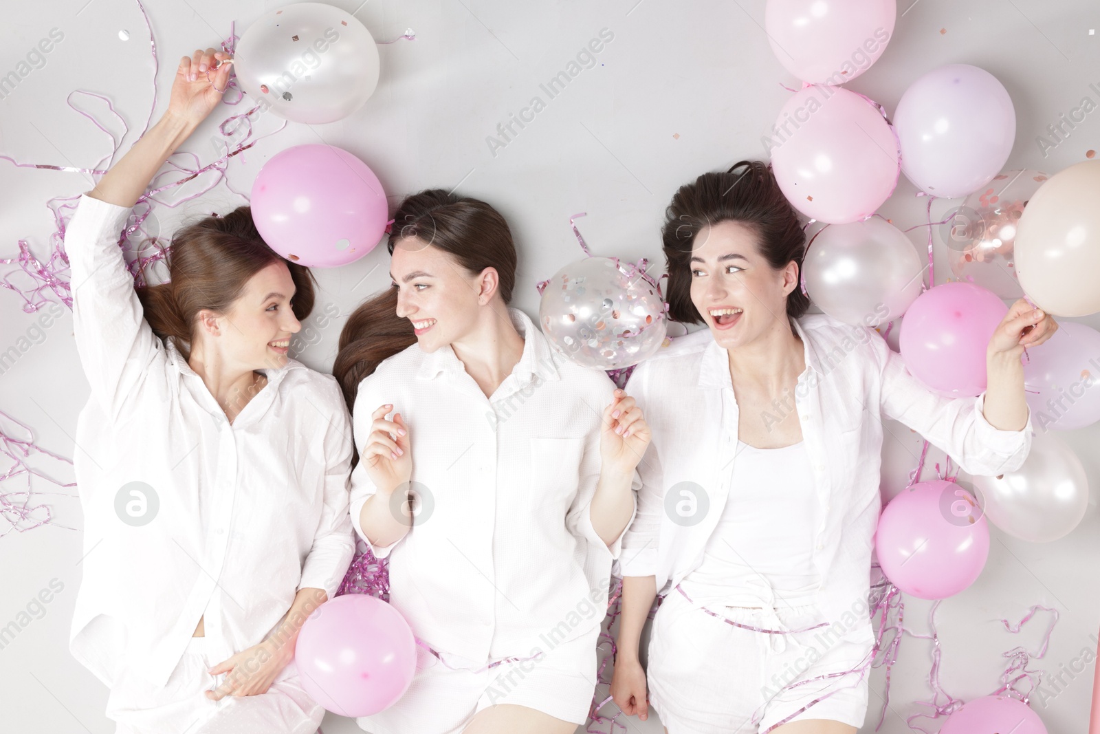 Photo of Pajama party. Happy friends with balloons and tinsel on grey background, top view