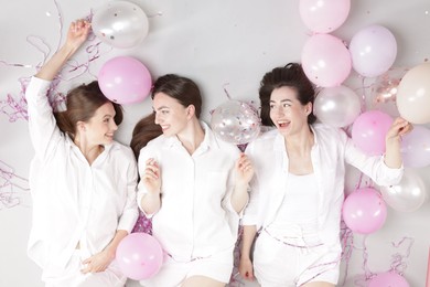 Photo of Pajama party. Happy friends with balloons and tinsel on grey background, top view