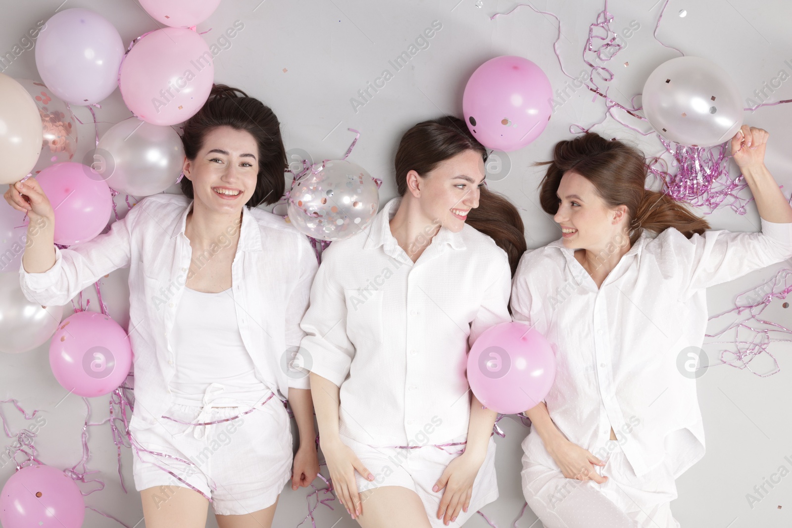 Photo of Pajama party. Happy friends with balloons and tinsel on grey background, top view