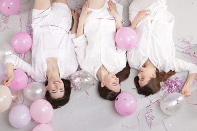 Photo of Pajama party. Happy friends with balloons and tinsel on grey background, above view