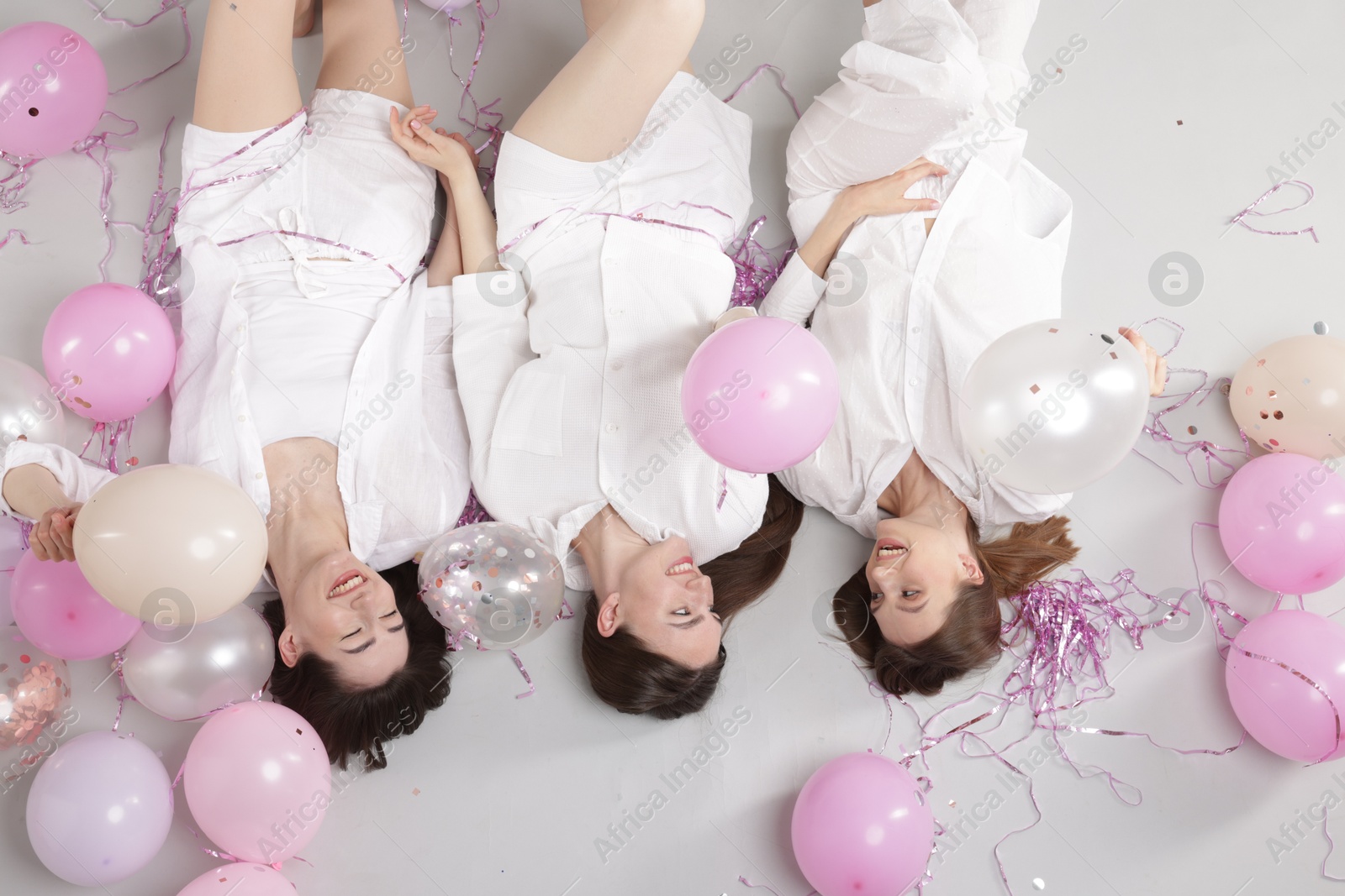 Photo of Pajama party. Happy friends with balloons and tinsel on grey background, above view