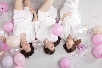 Photo of Pajama party. Happy friends with balloons and tinsel on grey background, above view