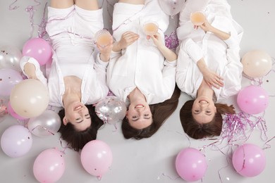 Photo of Pajama party. Happy friends with glasses of alcoholic drink, balloons and tinsel on grey background, top view