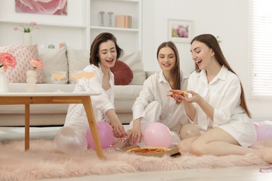Photo of Happy friends in pajamas eating pizza on floor at home