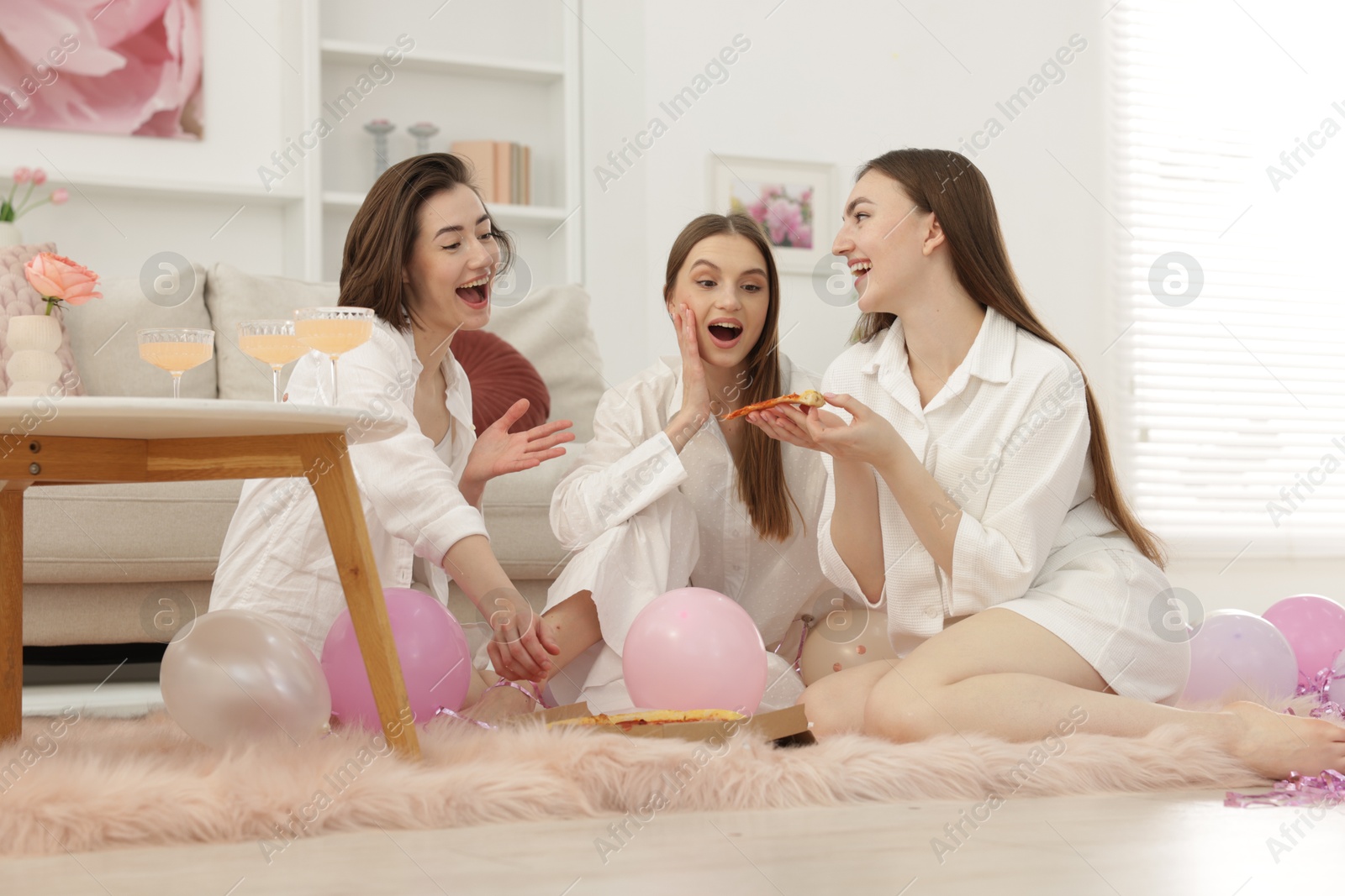 Photo of Happy friends in pajamas eating pizza on floor at home