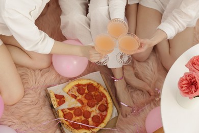 Photo of Pajama day. Friends with glasses of alcoholic drink and pizza on faux fur, above view