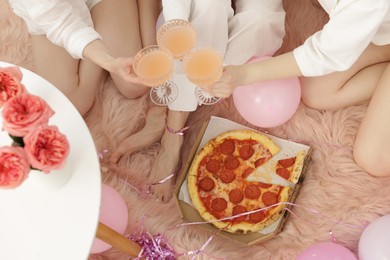 Photo of Pajama day. Friends with glasses of alcoholic drink and pizza on faux fur, above view