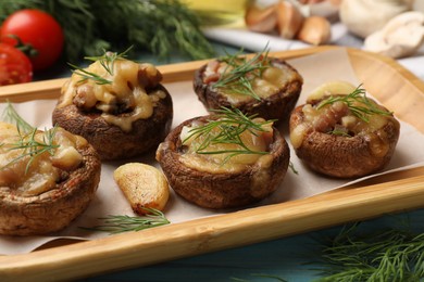 Photo of Delicious stuffed mushrooms with melted cheese, garlic and dill on light blue wooden table, closeup