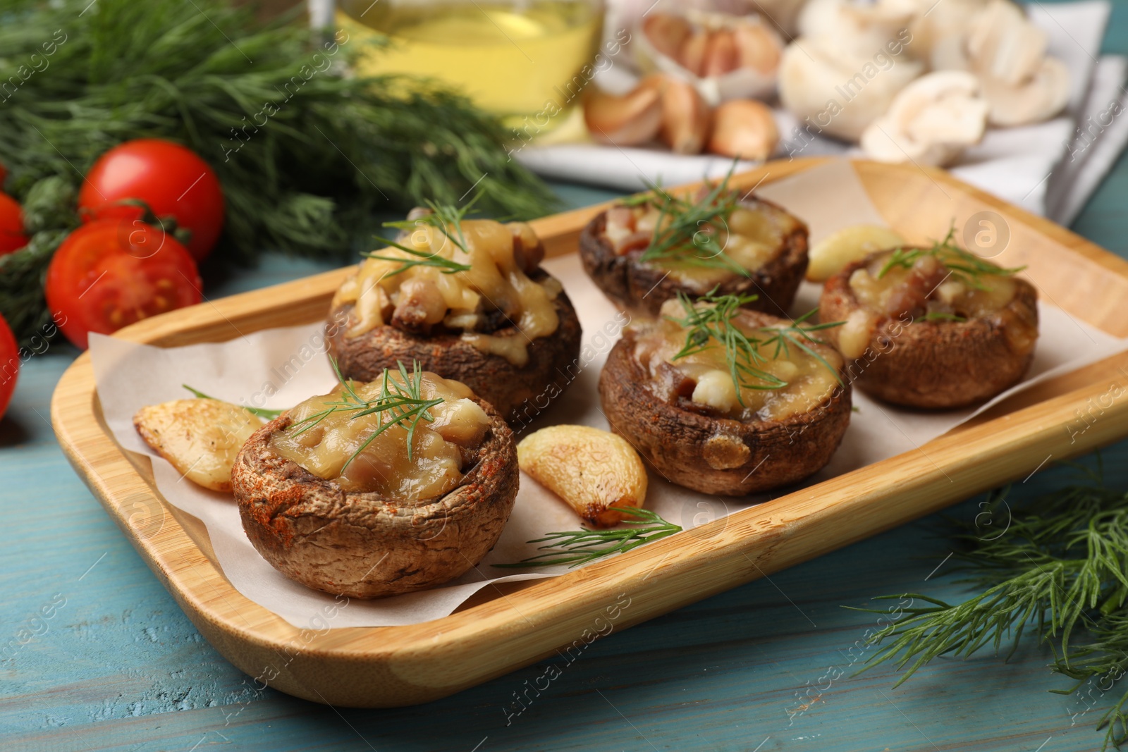 Delicious stuffed mushrooms with melted cheese, garlic and dill on light blue wooden table, closeup Photo of Delicious stuffed mushrooms with melted cheese, garlic and dill on light blue wooden table, closeup
