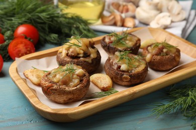 Photo of Delicious stuffed mushrooms with melted cheese, garlic and dill on light blue wooden table, closeup
