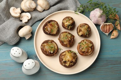 Photo of Delicious stuffed mushrooms with melted cheese, thyme and spices on light blue wooden table, flat lay