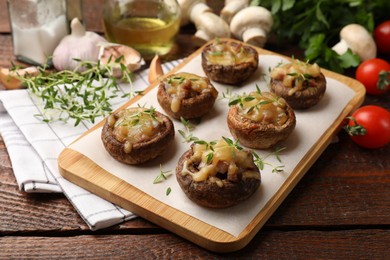 Photo of Delicious stuffed mushrooms with melted cheese and thyme on wooden table, closeup