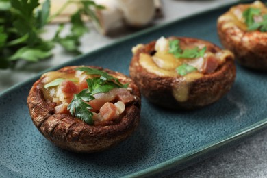 Photo of Delicious stuffed mushrooms with melted cheese and parsley on grey textured table, closeup