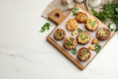 Photo of Delicious stuffed mushrooms with melted cheese, garlic and parsley on white marble table, flat lay. Space for text