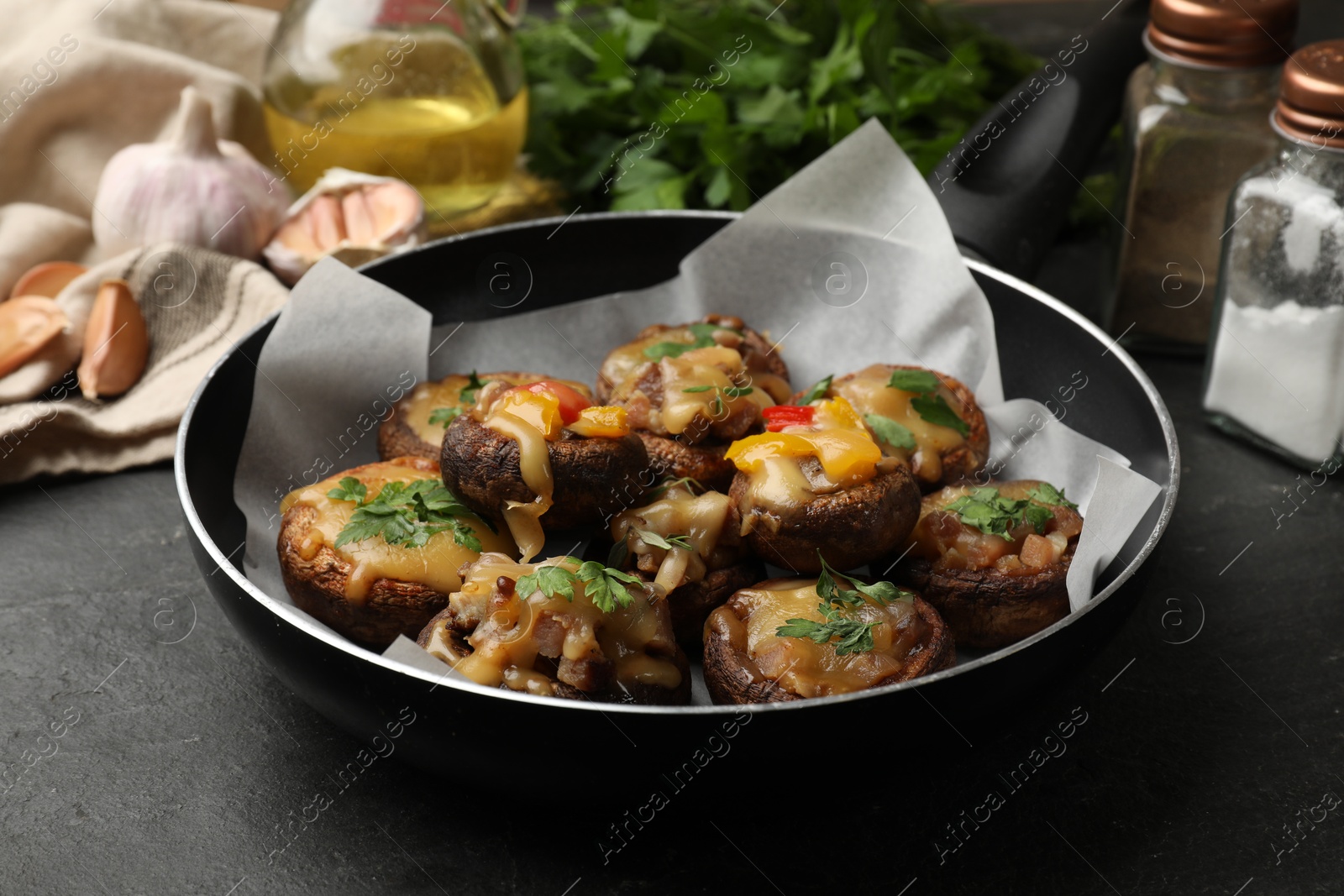 Tasty stuffed mushrooms in frying pan and ingredients on black table, closeup Photo of Tasty stuffed mushrooms in frying pan and ingredients on black table, closeup