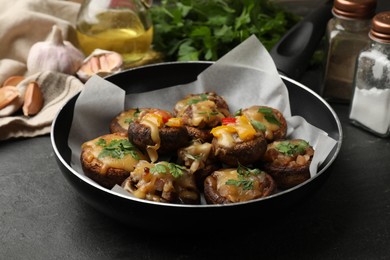 Photo of Tasty stuffed mushrooms in frying pan and ingredients on black table, closeup