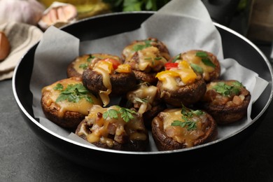 Photo of Tasty stuffed mushrooms in frying pan on black table, closeup