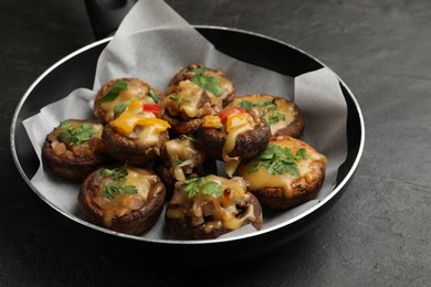 Photo of Tasty stuffed mushrooms in frying pan on black table, closeup