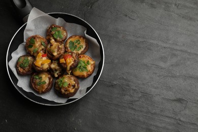 Photo of Tasty stuffed mushrooms in frying pan on black table, top view. Space for text