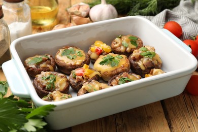 Photo of Tasty stuffed mushrooms in baking dish and ingredients on wooden table, closeup