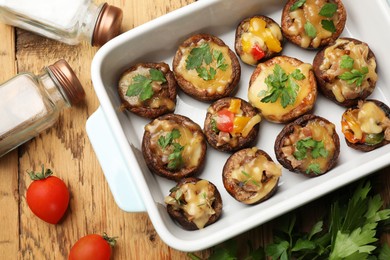 Photo of Tasty stuffed mushrooms in baking dish and ingredients on wooden table, flat lay