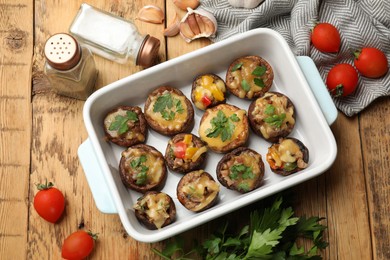 Photo of Tasty stuffed mushrooms in baking dish and ingredients on wooden table, flat lay